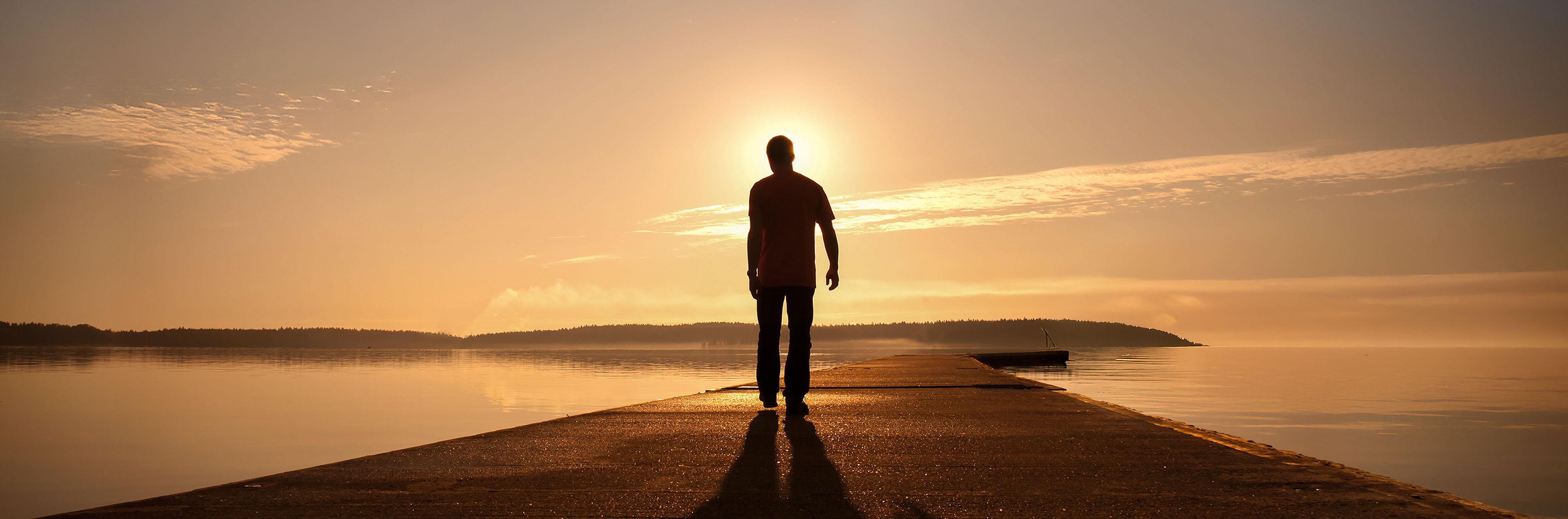 Eine Person geht einem Sonnenuntergang entgegen – Symbol für Abschied und Neubeginn
