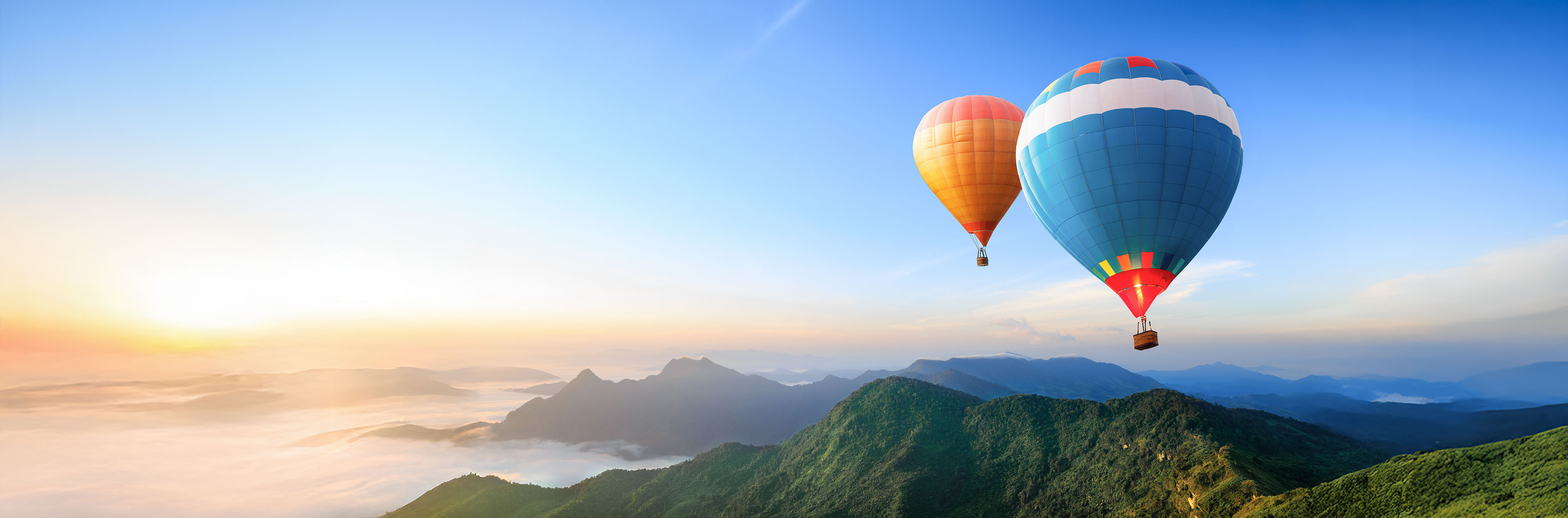Zwei Heißluftballons schweben über einer bergigen Landschaft im Morgenlicht